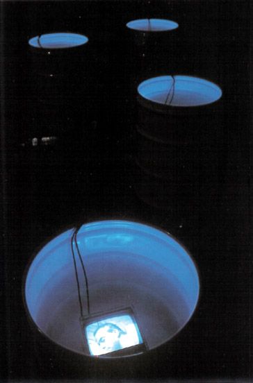Videoinstalación con barriles llenos de agua con pantallas sumergidas que muestran personas dormidas