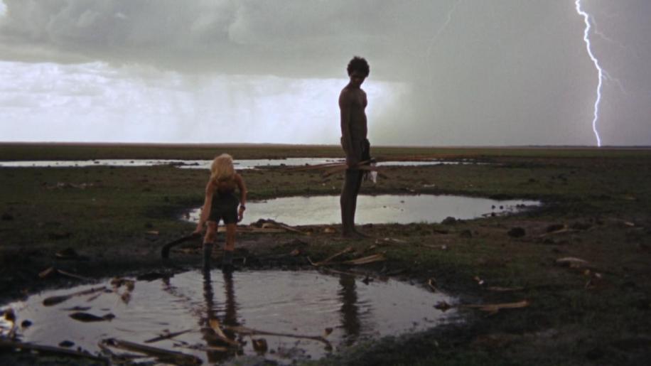 El aborigen mira al niño jugar en los charcos en medio de la tormenta