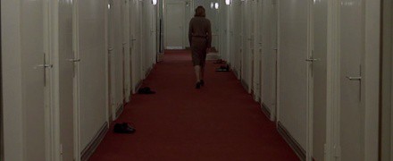 La protagonista se aleja por un pasillo con moqueta roja