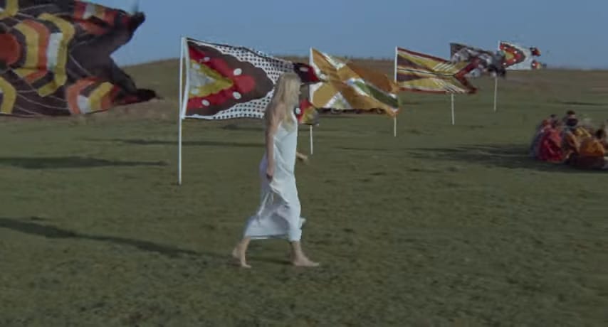 La protagonista deambula entre grupos de apariencia tribal americana y banderas coloridas al viento