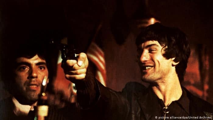 El protagonista apunta al usurero ante el asombro de su guardaespaldas