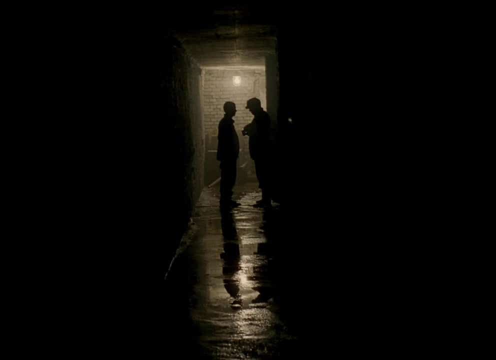 Dos de los prisioneros discuten en un pasadizo como sombras