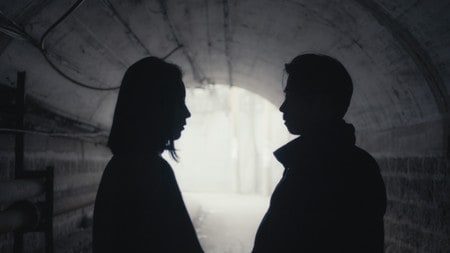 Las sombras recortadas de un hombre y una mujer hablan bajo un puente