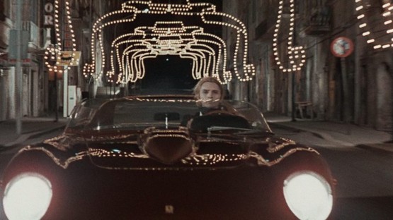 El protagonista conduce un descapotable rojo por una calle engalanada con luces de Navidad