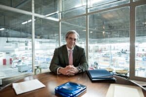 El protagonista sonríe desde su acristalado despacho, a sus espaldas la fábrica