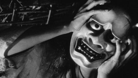 El protagonista sujeta una máscara horrorosa con grandes ojos y dientes