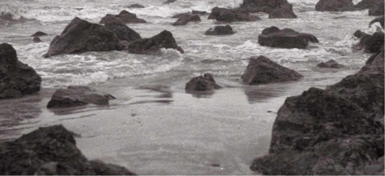 Unas olas baten sobre unas rocas y la arena de una playa