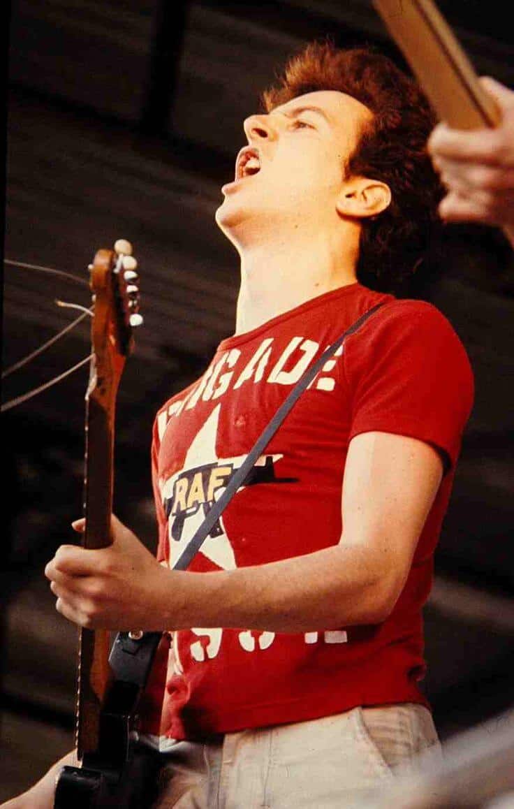 El cantante toca la guitarra con una camiseta con logos de los grupos armados