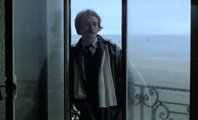 El protagonista entra por la puerta acristalada desde la playa brumosa