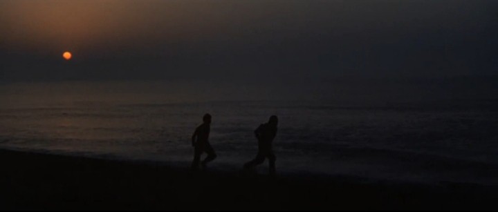 Los protagonistas huyen por una playa al caer el Sol