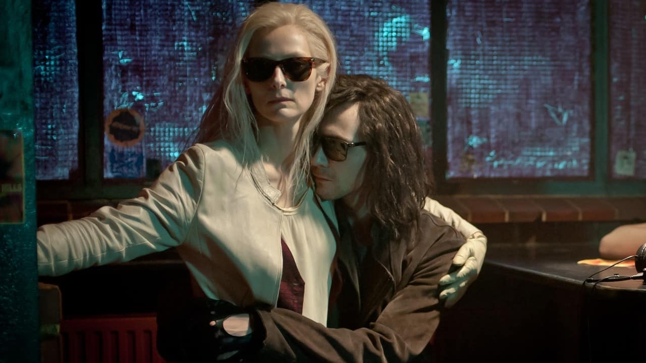 La pareja protagonista sentada en un bar con gafas de sol de noche
