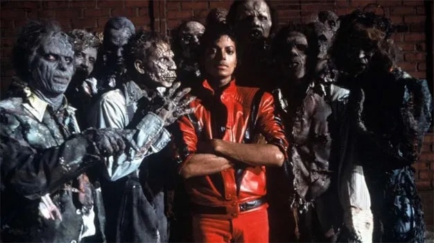 El cantante viste de brillante cuero rojo mientras le rodea un grupo de zombis macilentos