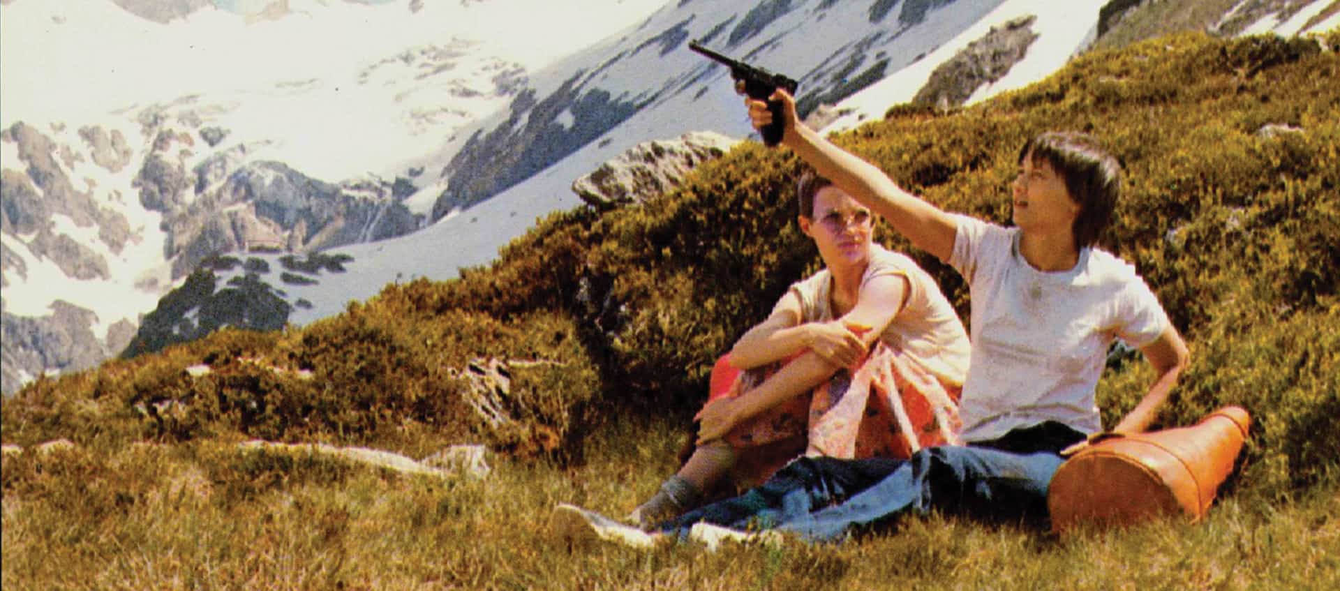 Una de las dos protagonistas levanta una pistola hacia el cielo sentadas en un prado