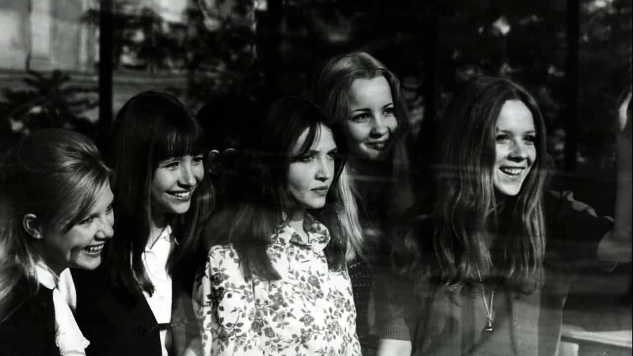 El grupo de las protagonistas ríe detrás de una gran ventana