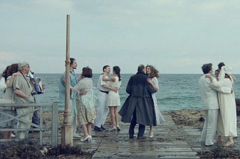 Los protagonistas bailan en una fiesta entre otras parejas al borde del mar