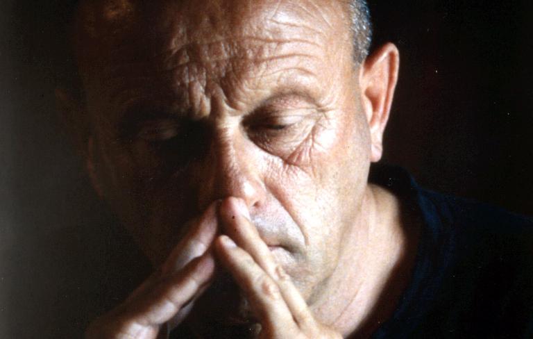 El protagonista, medio escondido en las sombras, reflexiona con las manos cruzadas