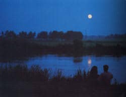 Una pareja ve pasar el río a la luz de la luna