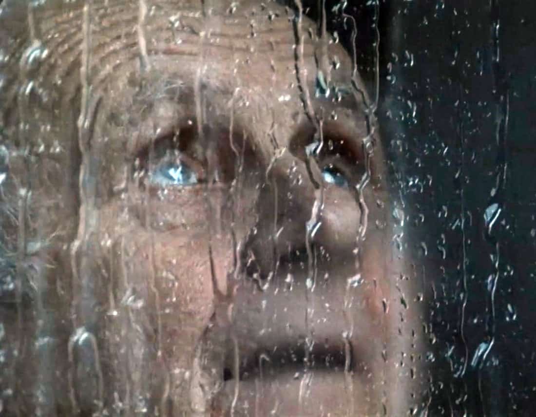 Un anciano mira a través de la ventana como cae una lluvia torrencial