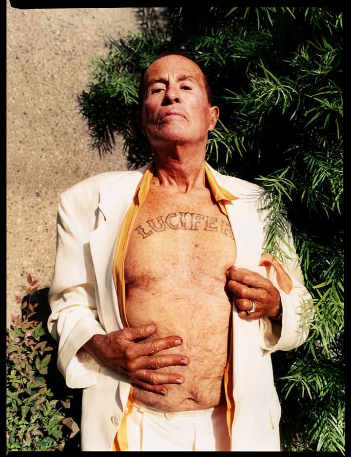 El artista abriéndose la chaqueta y mostrando un tatuaje del nombre del demonio
