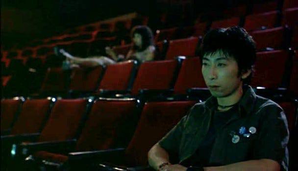 El protagonista está sentado en un cine casi vacío con una inquietante presencia detrás